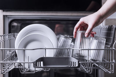 Female hand loading dished, empty out or unloading dishwasher with utensils. kitchen appliances