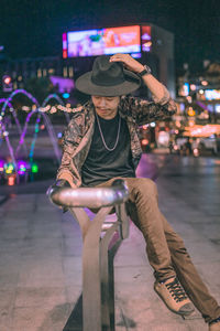 Portrait of man sitting on illuminated street at night