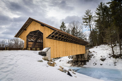 Covered bridge over river against sky during winter