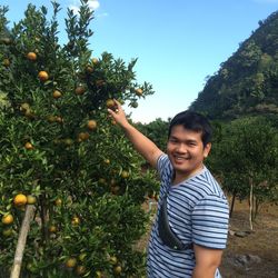 Portrait of smiling man holding oranges at farm against sky