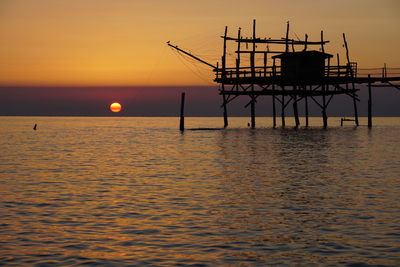 Silhouette built structure over sea against sky during sunset