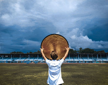 Rear view of boy standing by grass against sky