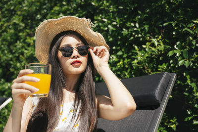 Portrait of young woman holding juice while sitting outdoors