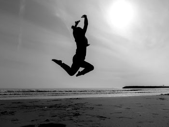 Silhouette man jumping at beach against sky