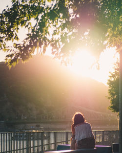 Rear view of woman standing by railing against sky during sunset