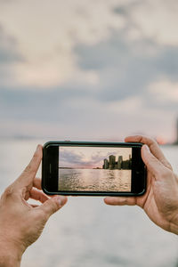 Cropped image of hand holding smart phone against sky