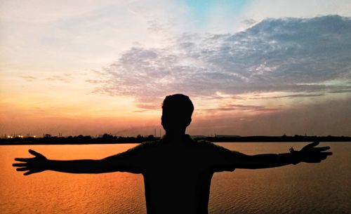 Rear view of silhouette person standing by sea against sky during sunset