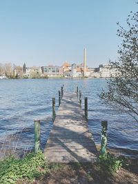 Footpath by river and buildings against clear sky