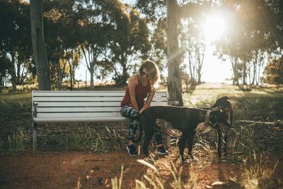 Woman with dog sitting on grass against trees