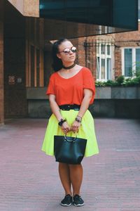 Full length of young woman holding purse while standing on walkway