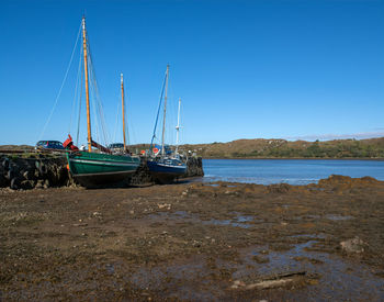 Sailboats moored on sea against clear blue sky