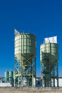 Low angle view of industrial silos against blue sky
