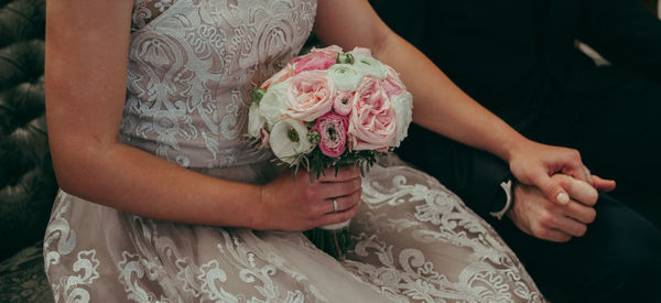 Midsection of bride holding bouquet and groom hand