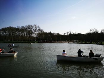 People sitting on riverbank against sky