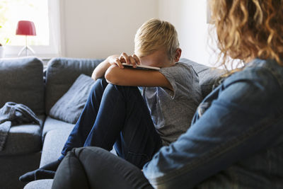 Sad son sitting with mother on sofa at home