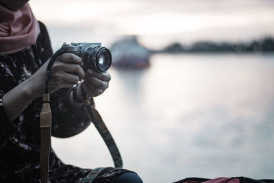 Midsection of person photographing with camera by sea