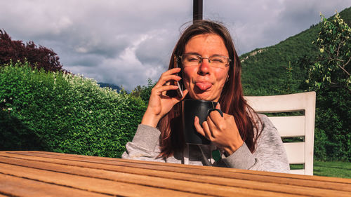 Portrait of woman talking on phone while making face sitting outdoors