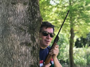 Portrait of young man wearing sunglasses against tree trunk