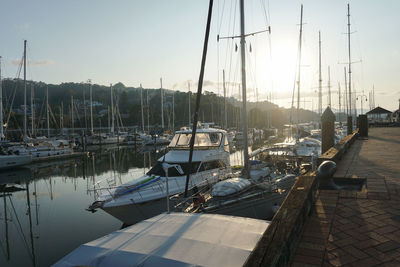 Sailboats moored at harbor against sky during sunset