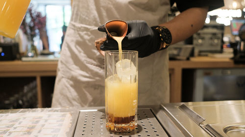 Midsection of man pouring orange in glass