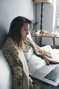 Sick young woman using laptop on bed at home
