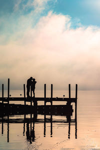 Silhouette man standing on pier by sea against sky during sunset