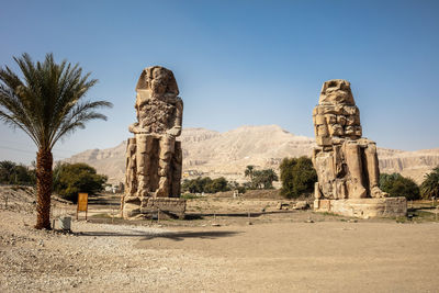 Beautiful daytime view of the colossi of memnon. two large stone figures depicting a seated pharaoh.