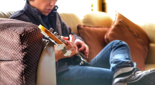 Midsection of man playing guitar on sofa at home