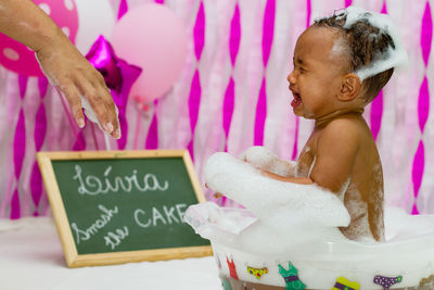 Cropped hand of parent by shirtless crying baby in tub during first birthday