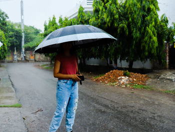 Full length of woman walking on wet road during rainy season