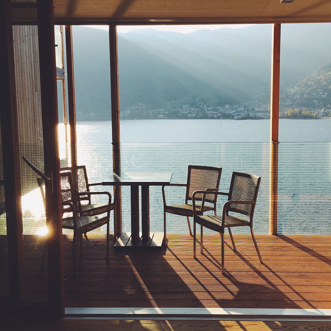 water, mountain, sea, railing, sunlight, tranquility, sky, sunset, built structure, nature, scenics, beauty in nature, tranquil scene, mountain range, chair, absence, bench, indoors, pier, empty