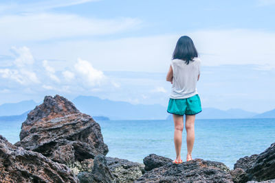 Rear view of woman standing on rock at beach against sky