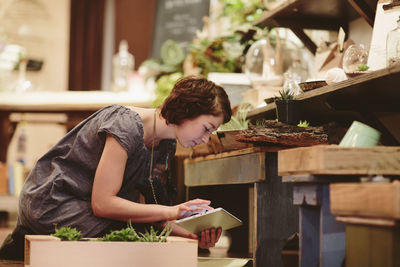 Female worker using tablet computer while examining plants at garden center