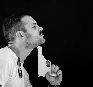 Shirtless man attempting suicide with gun against black background