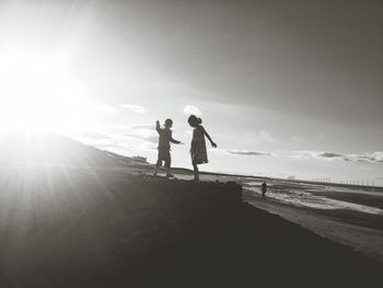 Silhouette of boy and girl standing at beach against sky during sunset