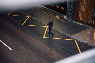 High angle view of businessman using mobile phone while walking on city street