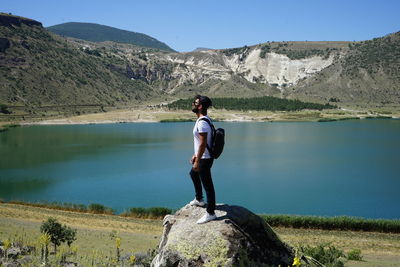 Full length of man standing on rock by lake against sky