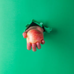 Close-up of hand holding apple against blue background