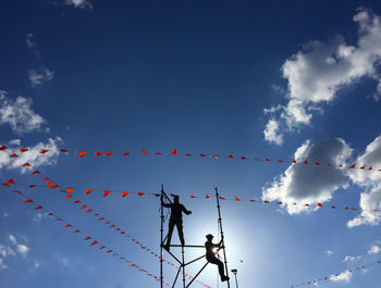 Low angle view of men on metallic structure against blue sky