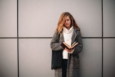 Portrait of young woman standing against wall