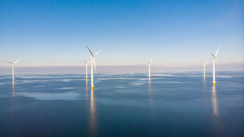 Windmills on field against clear blue sky