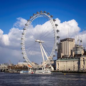 Ferris wheel in city against cloudy sky