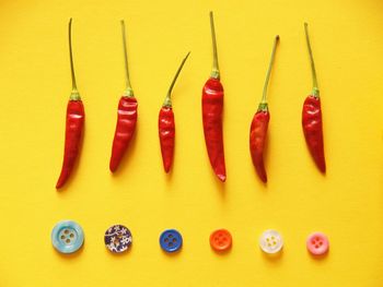 High angle view of red chili pepper with colorful buttons arranged on yellow background