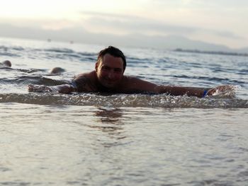 Portrait of man lying at beach against sky