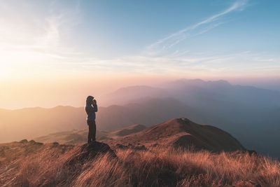 Side view of tourist standing on mountain against sky during sunset