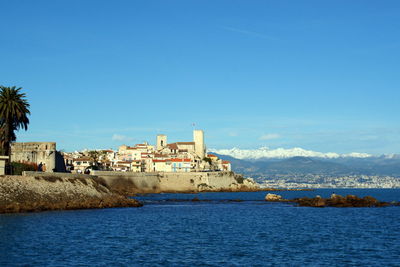 Buildings by sea against clear blue sky