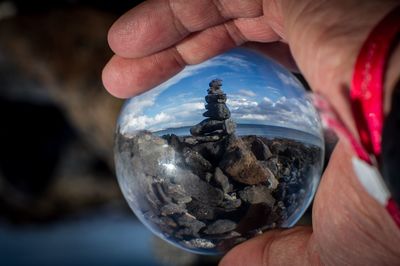 Cropped hand holding crystal ball with rocks and sea reflection