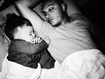 Close-up of father with baby sleeping on bed