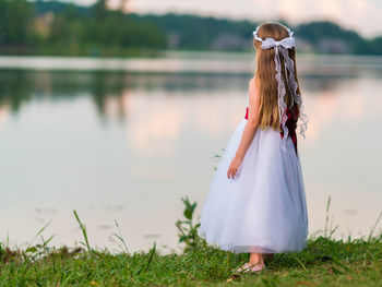 Rear view of girl standing at lakeshore during sunset