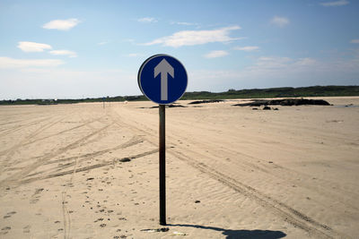 Road sign on beach against sky